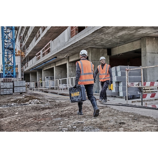 Two workers on a conctruction site; one worker carries a Dewalt tool case and one worker carries Powershift 554WH battery