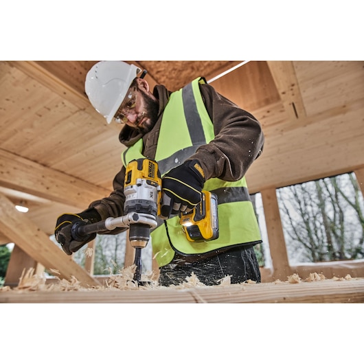 Side shot of construction worker using 18V XR Brushless Premium Hammer Drill Driver with 5Ah Powerstack to drill a hole in wood