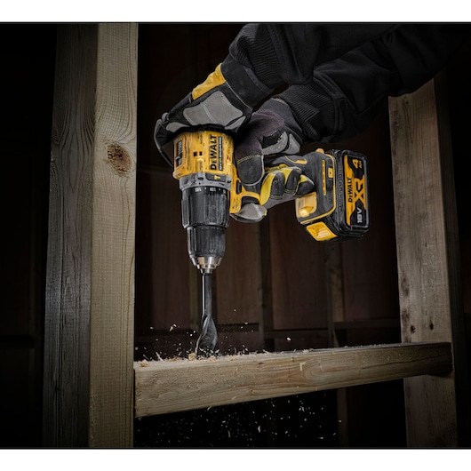 close up view of the DCD100 drilling through timber stud wall using both hands