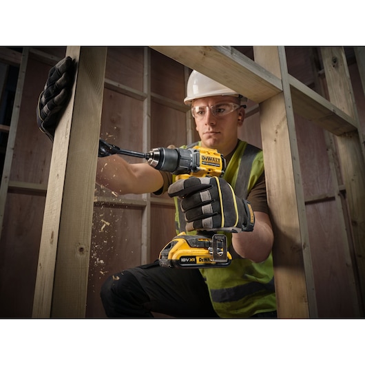 18V XR Brushless Compact Hammer Drill Driver with 18V 2Ah battery used by worker to drill wooden frame