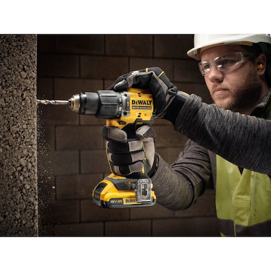 18V XR Brushless Compact Hammer Drill Driver with 18V 2Ah battery used by worker to drill concrete frame