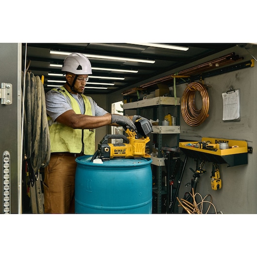 DEWALT 18V XR Transfer Pump connected by worker to a drum, worker is adding battery