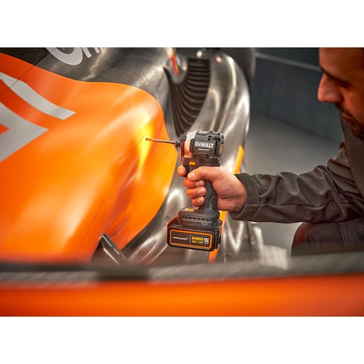 McLaren mechanic using DEWALT/McLaren impact driver on side panel of racing car