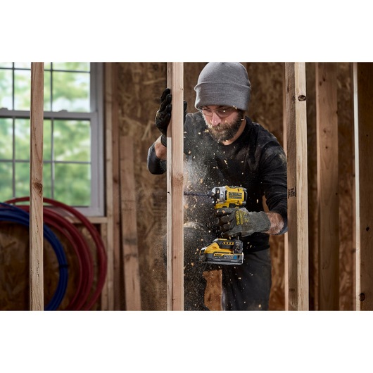 Construction worker uses 18V XR 4 Speed Premium Impact Driver to drill a hole into wooden stud wall