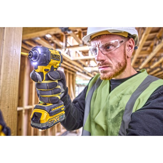 Worker using DCF870 18V XR Brushless impact driver to drive into a wooden frame. Tool work lights are illuminated
