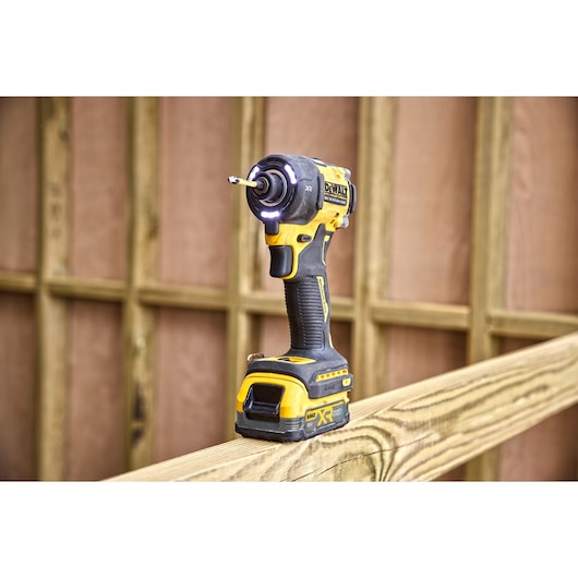 DCF870 18V XR Brushless impact driver sitting on top of a wooden beam. Tool work lights are illuminated.