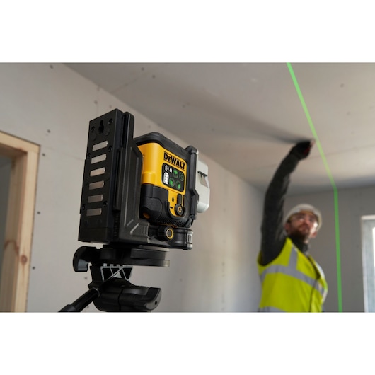 The DEWALT 3x 180 USB Green Beam Laser in foreground attached to tripod, helping to guide the worker mark up the ceiling.