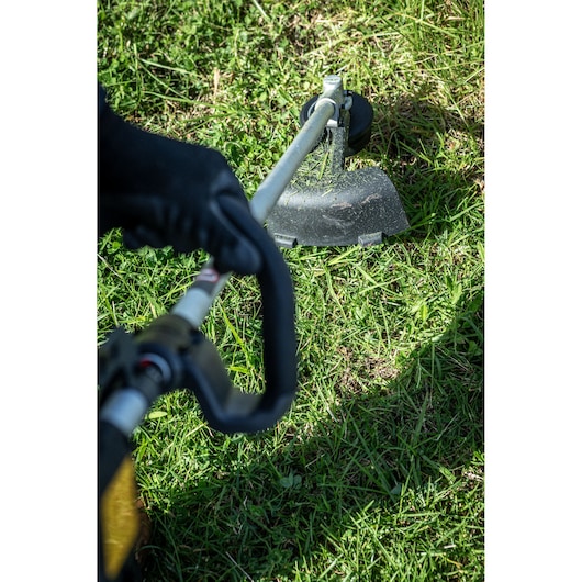 Close view of worker using the DEWALT 54V String Trimmer (D-Handle) near to barbed wire fence