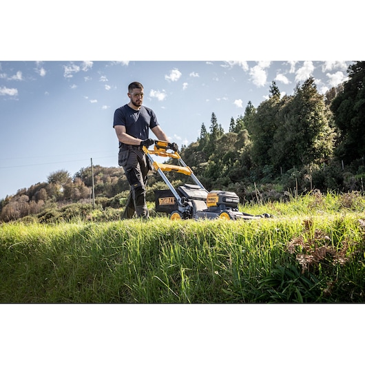 The DEWALT 54V 53cm Self-Propelled Mower being used by landscaper for maintenance in large area, landscaper wearing safety goggles and gloves.
