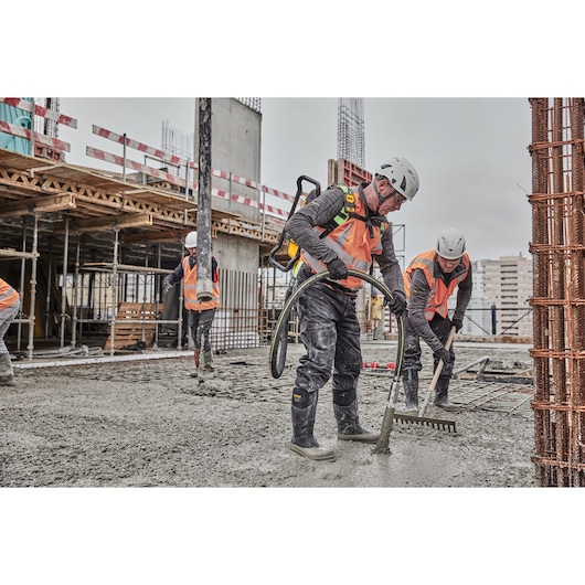 Workers pouring concrete on construction site. Worker closest to camera uses Powershift Backpack Concrete Vibrator