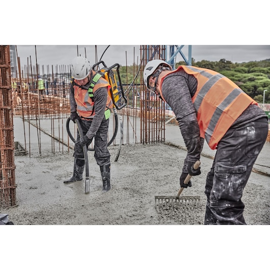 Worker pours concrete using Powershift Backpack Concrete Vibrator while another worker rakes out the concrete