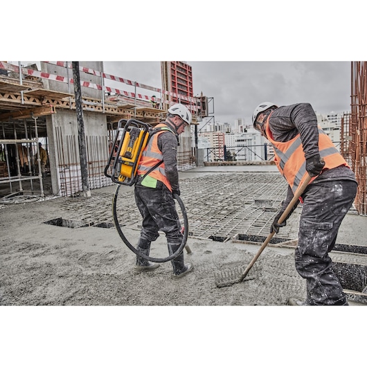 Two workers pouring and raking on concrete on a construction site. Concrete is being poured using Powershift Backpack Concrete Vibrator