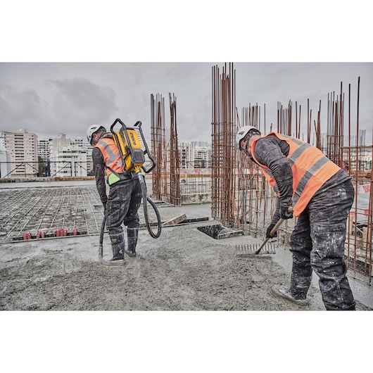 Two workers pouring and raking on concrete. Concrete is being poured using Powershift Backpack Concrete Vibrator