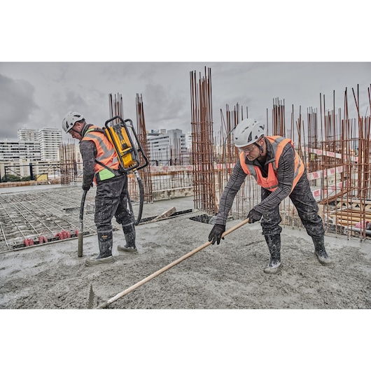 Workers pouring and raking on concrete. Concrete is being poured using Powershift Backpack Concrete Vibrator