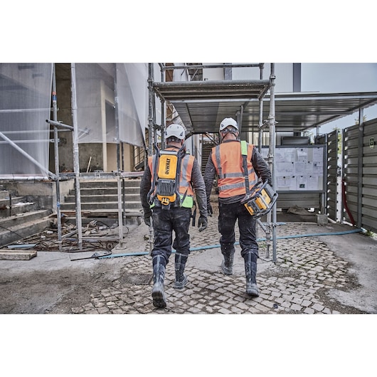 Two construction workers walking off site. Each carries a Powershift Backpack Concrete Vibrator