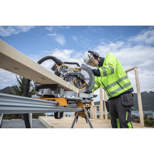 The DEWALT 18V XR 305mm Slide Mitre Saw being used by worker with safety goggles, hat and ear defenders to cut through timber beam outdoors