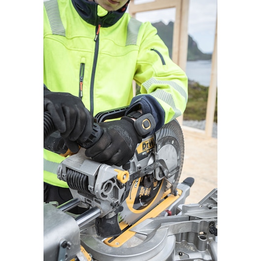 The DEWALT 18V XR 305mm Slide Mitre Saw being used by worker with safety goggles, hat and ear defenders to cut through timber beam outdoors