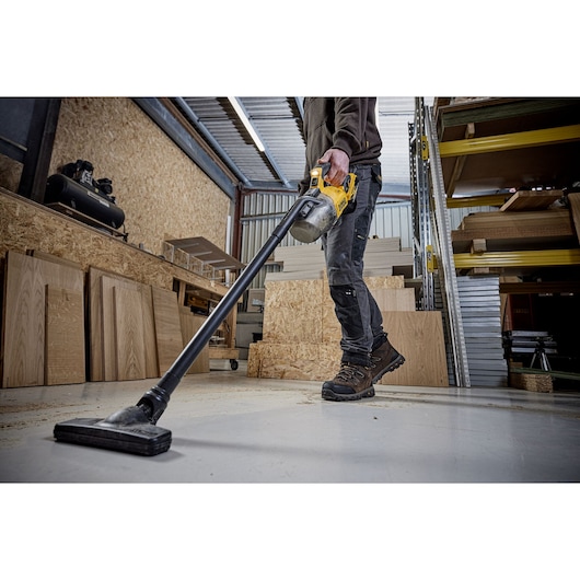 A CARPENTER USING A DCV501L 18V XR L-CLASS STICK VAC TO CLEAN THEIR WORK SHOP FLOOR