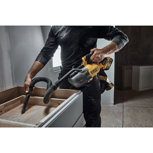 A CARPENTER USING A DCV501L 18V XR L-CLASS STICK VAC TO CLEAN A KITCHEN CABINET