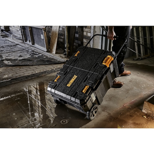 Construction worker pulling a wet mobile TSTAK job chest through a puddle on a construction site