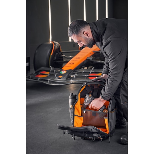 McLaren mechanic placing a drill driver into a DEWALT/McLaren backpack on wheels. A McLaren racing car is in the background