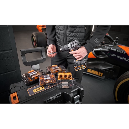 x4 Limited Edition DEWALT/McLaren screwdriver bit sets sit on top of a Tstak box, behing which a McLaren mechanic stands holding a impact driver and bit holder.
