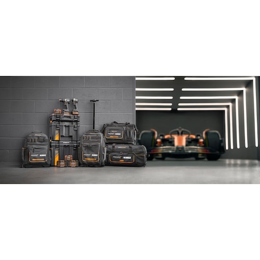 Limited Edition DEWALT/McLaren storage bags, Tstak trolley, impacts and accessory boxes stand in front of a grey wall. A McLaren racing car is on the right in the background.
