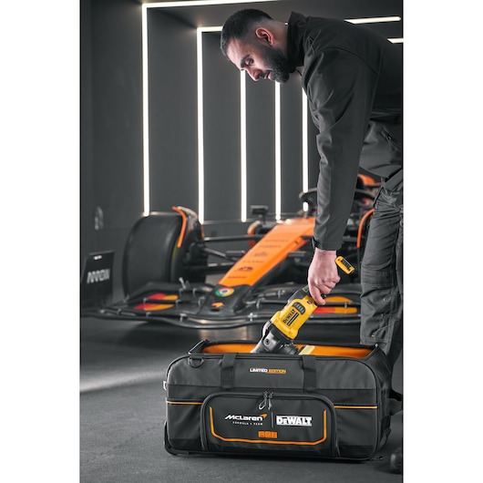 DEWALT tool being placed into a DEWALT/McLaren Duffle Bag DEWALT/McLaren Duffle Bag with wheels